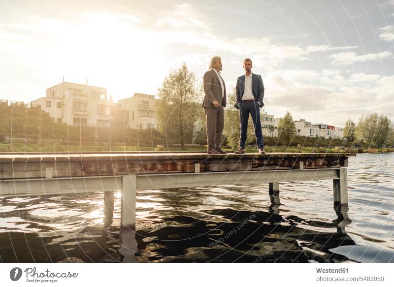Two businessmen standing on jetty at a lake jetties Businessman Business man Businessmen Business men lakes business people businesspeople business world