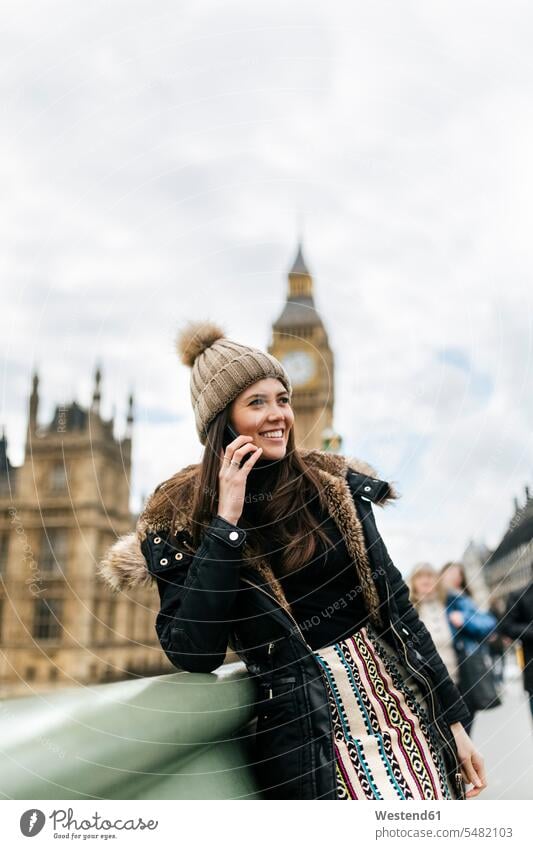 UK, London, happy young woman telephoning with smartphone in front of Palace of Westminster palace palaces City Break City Trip Urban Tourism woolly hat
