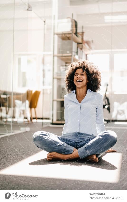 Happy young woman sitting on floor in office Seated relaxed relaxation females women laughing Laughter relaxing Adults grown-ups grownups adult people persons