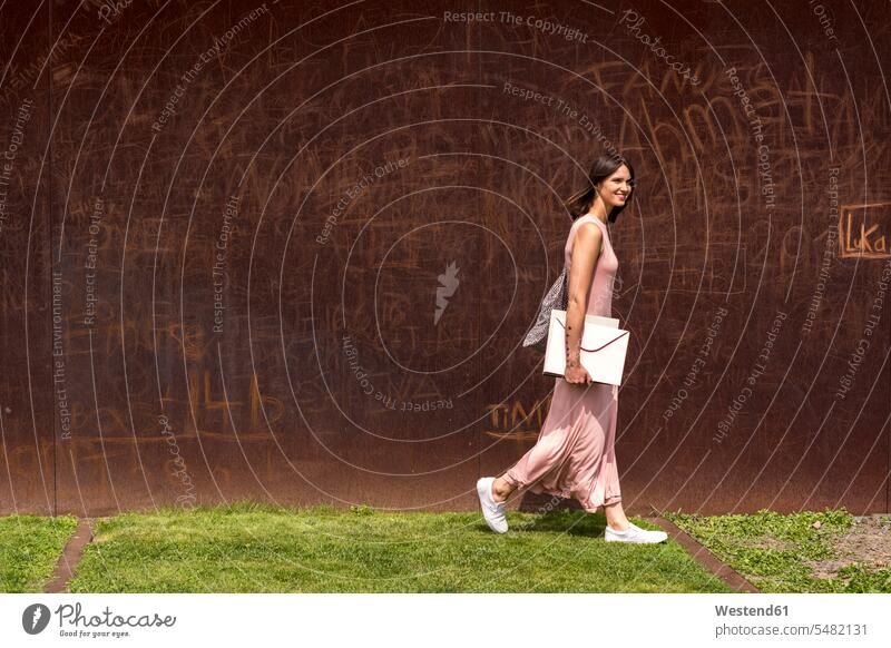 Smiling young woman walking in front of corten wall females women Adults grown-ups grownups adult people persons human being humans human beings folder file