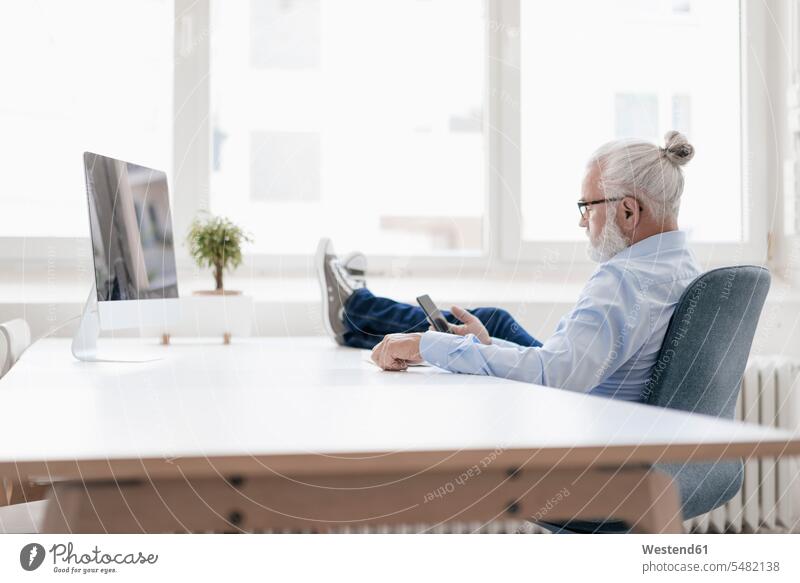Mature man with beard using cell phone at desk men males break relaxed relaxation Adults grown-ups grownups adult people persons human being humans human beings
