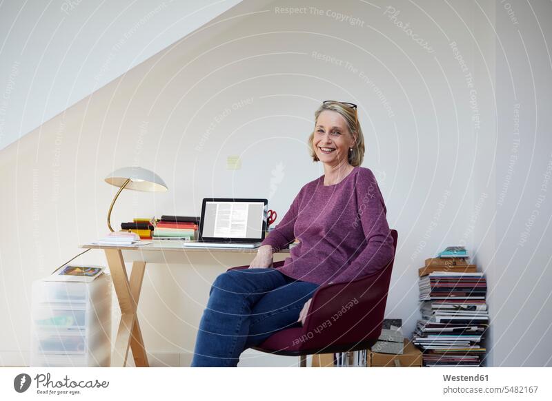 Portrait of smiling mature woman at home with laptop at desk Laptop Computers laptops notebook portrait portraits smile females women computer computers Adults