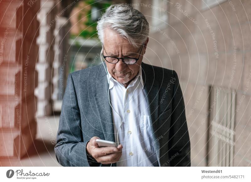 Senior businessman with earphones looking at cell phone Businessman Business man Businessmen Business men business people businesspeople business world