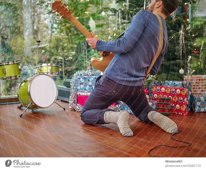 Man playing electric guitar in front of Christmas tree electric guitars exuberance hilarity Frolic exuberant copy space Imagination fantasy Phantasy imagining