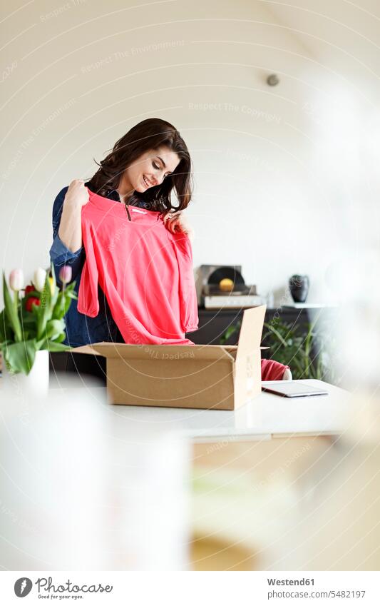 Smiling woman at home unpacking parcel with garment packet packets parcels clothing clothes smiling smile females women fashion fashionable Adults grown-ups