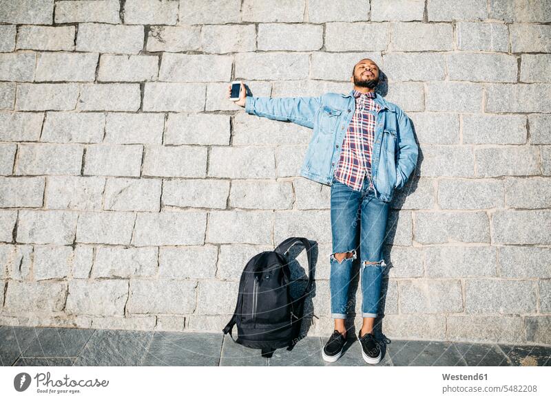 Young man standing in front of a wall holding cell phone Smartphone iPhone Smartphones men males mobile phone mobiles mobile phones Cellphone cell phones Adults
