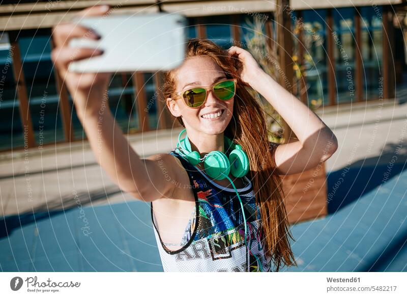 Smiling young woman wearing mirrored sunglasses taking selfie with smartphone Selfie Selfies females women Adults grown-ups grownups adult people persons
