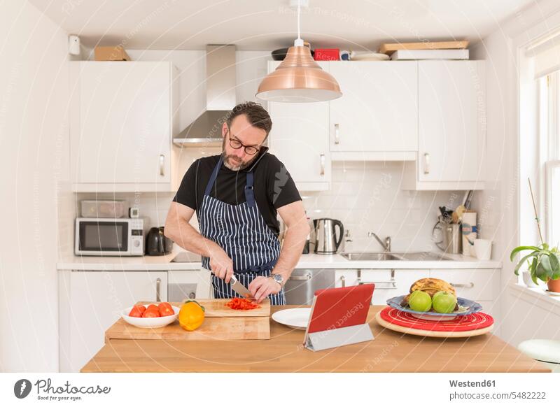 Man telephoning with smartphone while preparing vegetables in the kitchen listening food and drink Nutrition Alimentation Food and Drinks bell pepper Paprika