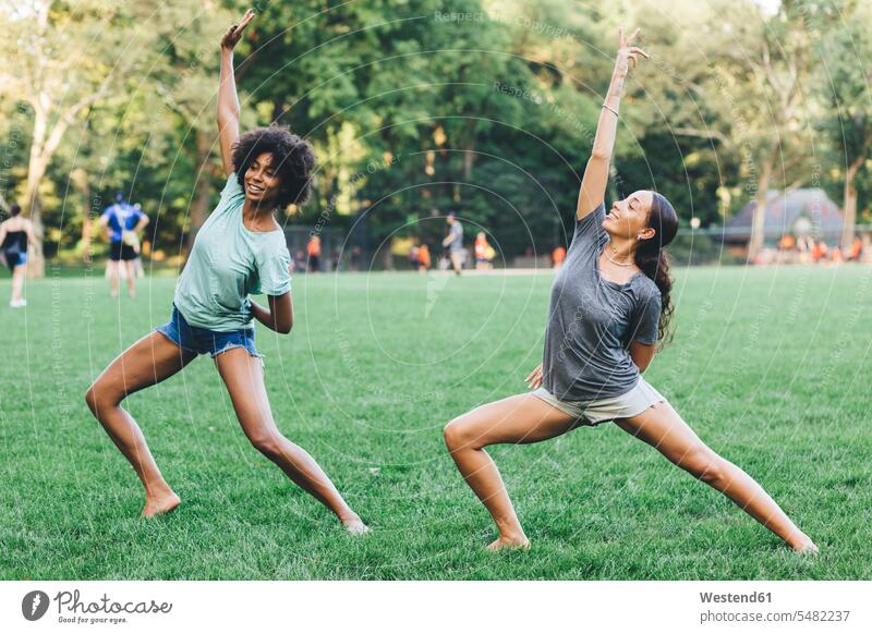 Two young women doing yoga exercise in a park female friends mate friendship mindfulness aware awareness self-care relaxation exercise relaxed relaxing