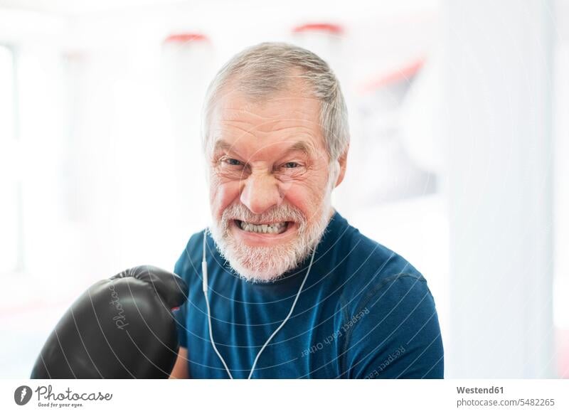 Portrait of aggressive senior man with earphones and boxing gloves in gym gyms Health Club senior men elder man elder men senior citizen exercising exercise