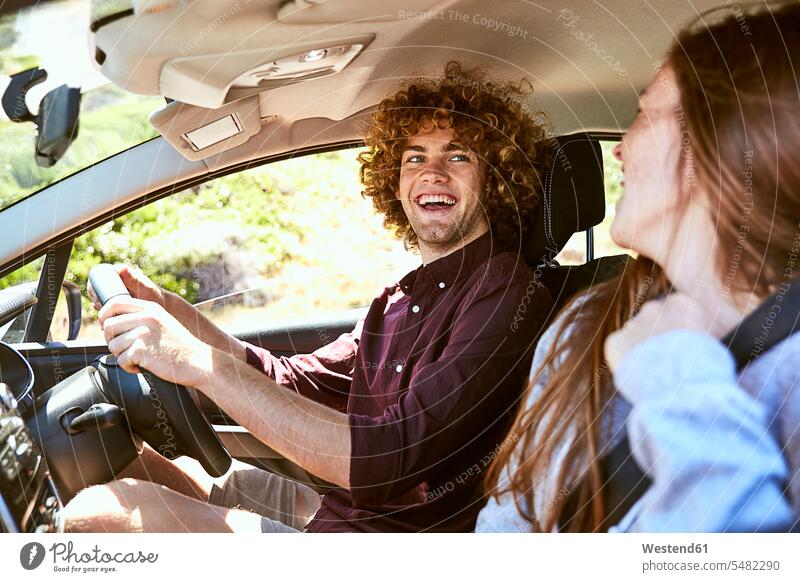 Laughing young man driving car looking at his girlfriend laughing Laughter couple twosomes partnership couples drive men males automobile Auto cars motorcars