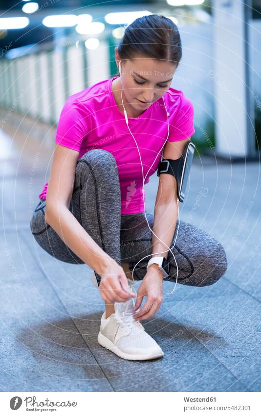 Young woman in pink sportshirt listening to music and tying her sneakers young women young woman Listening Music jogger joggers female jogger earphones