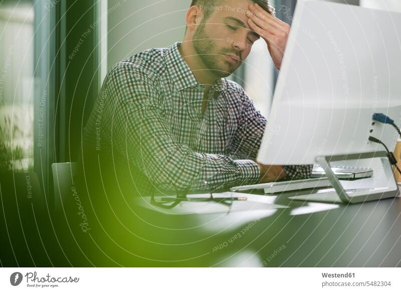 Tired young man at desk in office occupation profession professional occupation jobs Overstress Overexertion Overwork overstrained overworked overextended