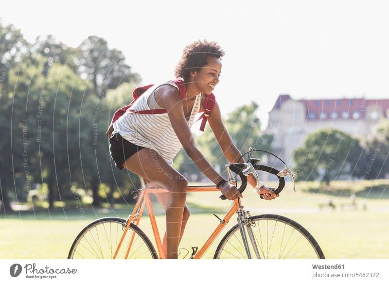 Smiling young woman riding bicycle in park driving drive bikes bicycles females women parks smiling smile Adults grown-ups grownups adult people persons