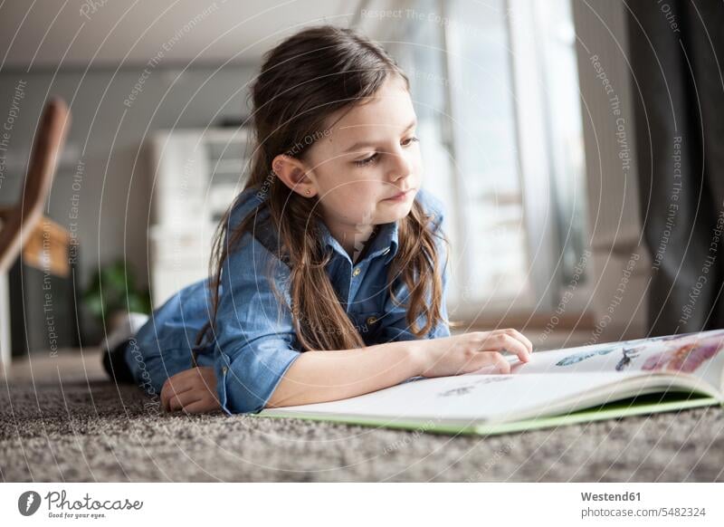 Portrait of little girl lying on the floor watching picture book Germany reader readers reading lying on front face-down prone position laying on front