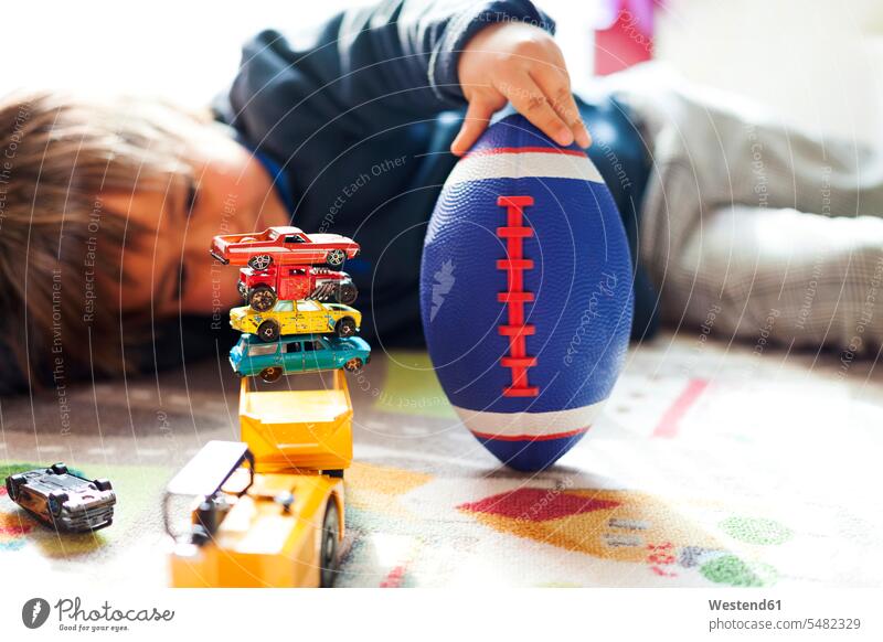 Boy lying on floor with football and stack of toy cars caucasian caucasian ethnicity caucasian appearance european laziness lazy rugby ball playing Football