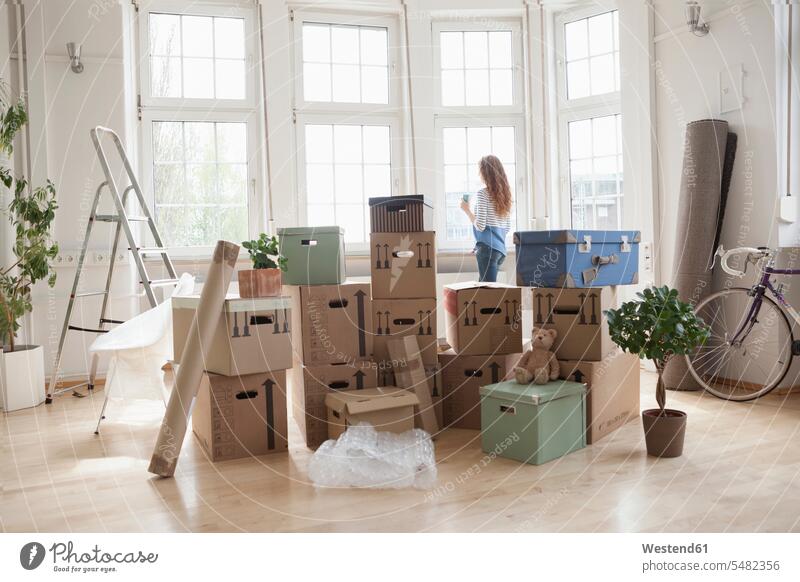 Woman with cardboard boxes in new apartment looking out of window flats apartments moving house move Moving Home moving in move in woman females women
