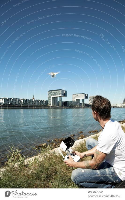 Mature man sitting in grass flying a drone unmanned aerial vehicle drones navigating navigate photographing Seated filming shooting men males watching observing