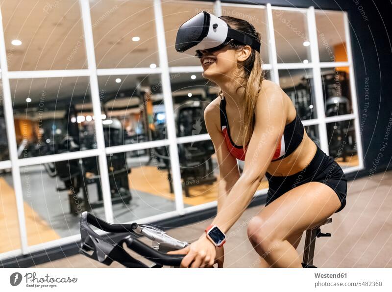 Woman with VR glasses on spinning bike in the gym woman females women Virtual Reality Glasses Virtual-Reality Glasses virtual reality headset vr headset