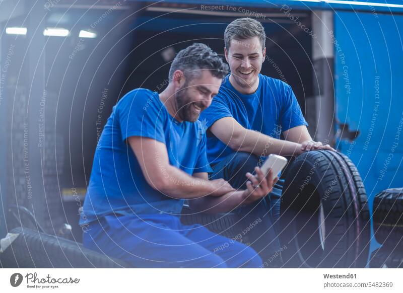 Two mechanics on a break looking at cell phone smiling smile sitting Seated man men males tire tyres tires mobile phone mobiles mobile phones Cellphone