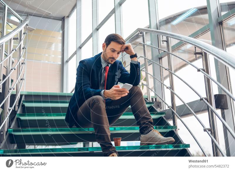 Pensive businessmann sitting on stairs looking at cell phone Businessman Business man Businessmen Business men message Smartphone iPhone Smartphones