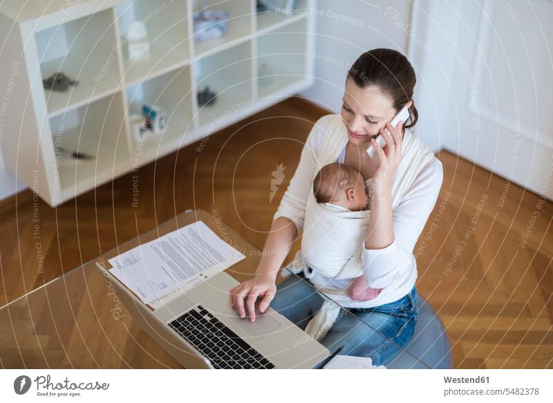 Mother with baby girl in sling working from home at home home office home business babies infants At Work on the phone call telephoning On The Telephone calling