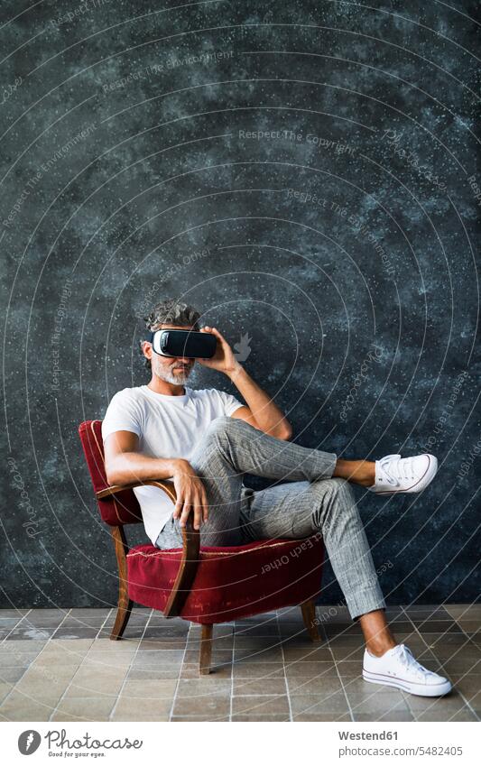 Mature man looking through VR glasses, sitting in armchair Arm Chairs armchairs eyeing watching looking at Virtual Reality Glasses Virtual-Reality Glasses