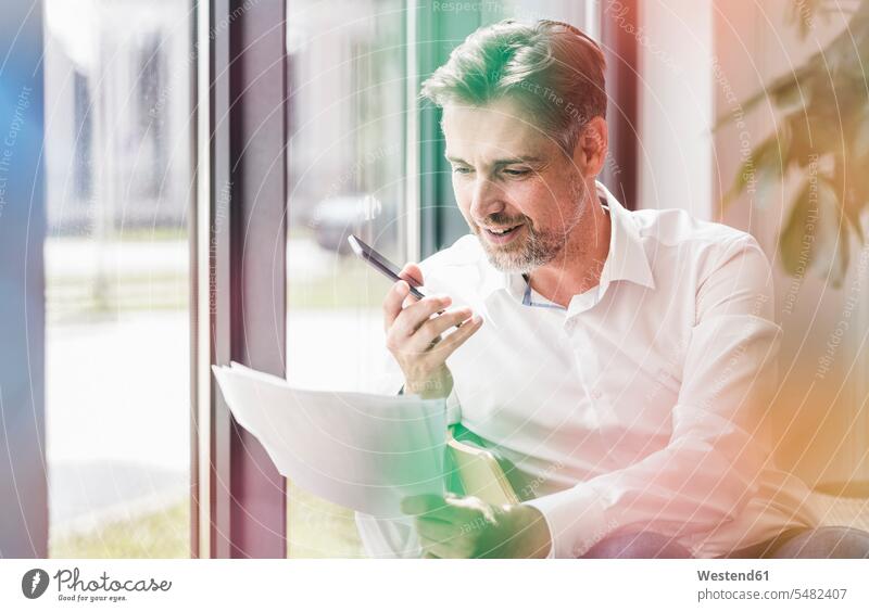 Businessman looking at documents using cell phone paper papers mobile phone mobiles mobile phones Cellphone cell phones Business man Businessmen Business men