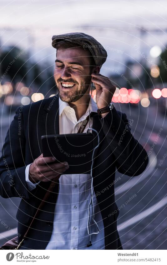 Happy young man in the city with earphones and tablet at dusk laughing Laughter smiling smile men males digitizer Tablet Computer Tablet PC Tablet Computers