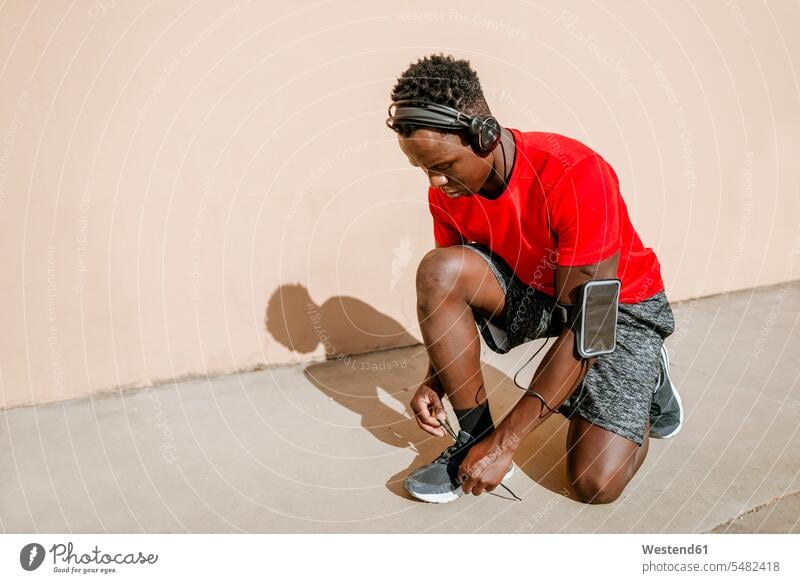 Man in sportswear tying his shoes while listening music with headphones headset man men males Adults grown-ups grownups adult people persons human being humans
