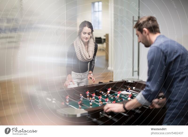 Two colleagues playing foosball in office break room table football table soccer sport sports offices office room office rooms workplace work place