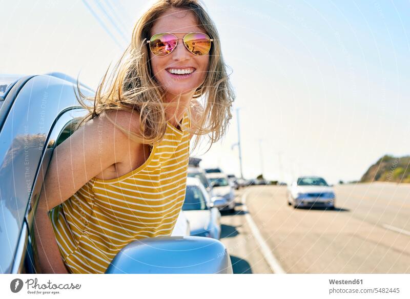 Happy young woman leaning out of car window automobile Auto cars motorcars Automobiles females women smiling smile motor vehicle road vehicle road vehicles