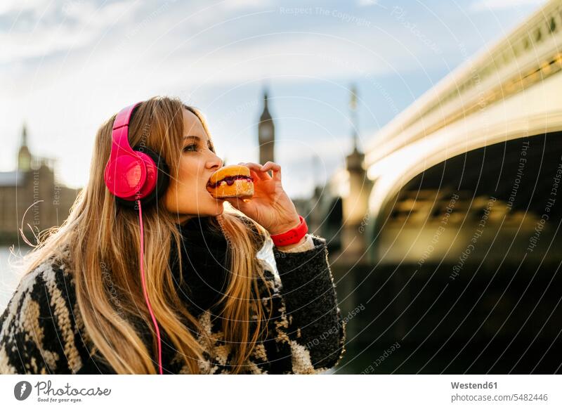 UK, London, young woman listening music and taking a snack near Westminster Bridge City Break City Trip Urban Tourism sky skies focus on foreground