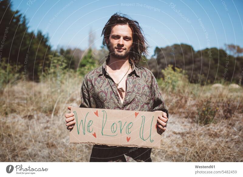 Hippie holding 'We love you' sign in the nature caucasian caucasian ethnicity caucasian appearance european beard natural world outdoors outdoor shots