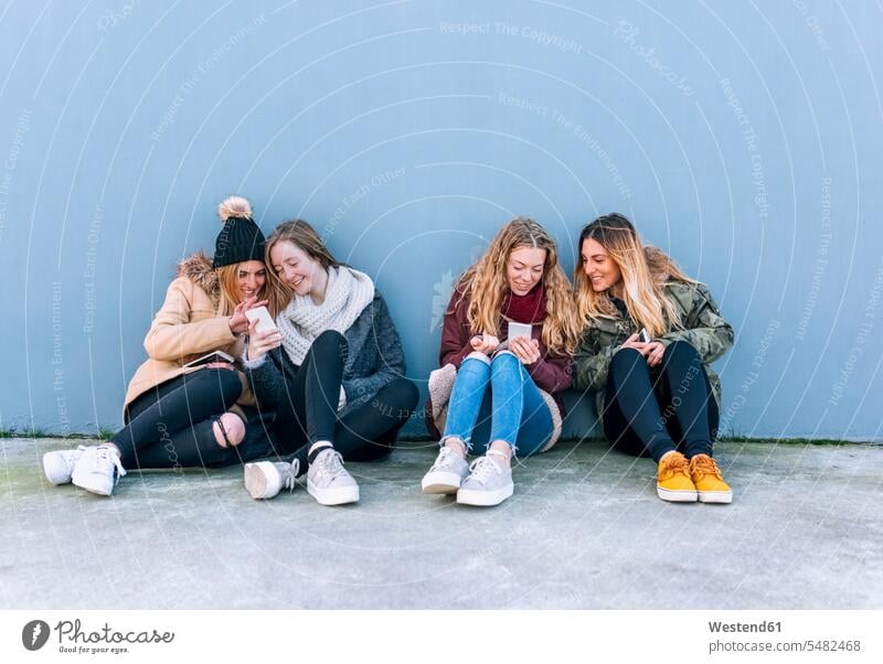 Four friends sitting side by side on the ground looking at cell phones mate female friend use telecommunication telephone telephones Cellphone mobile