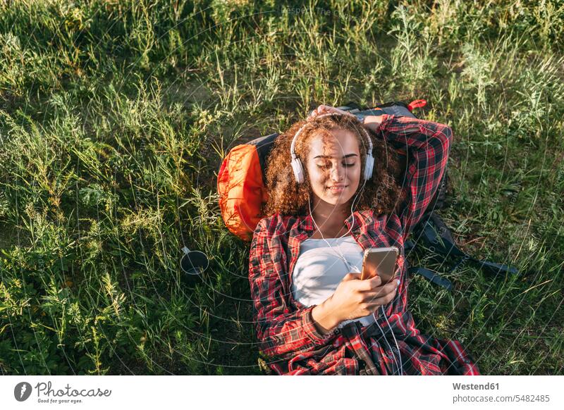 Teenage girl with backpack listening music with headphones and cell phone on a meadow lying laying down lie lying down Teenage Girls female teenagers headset