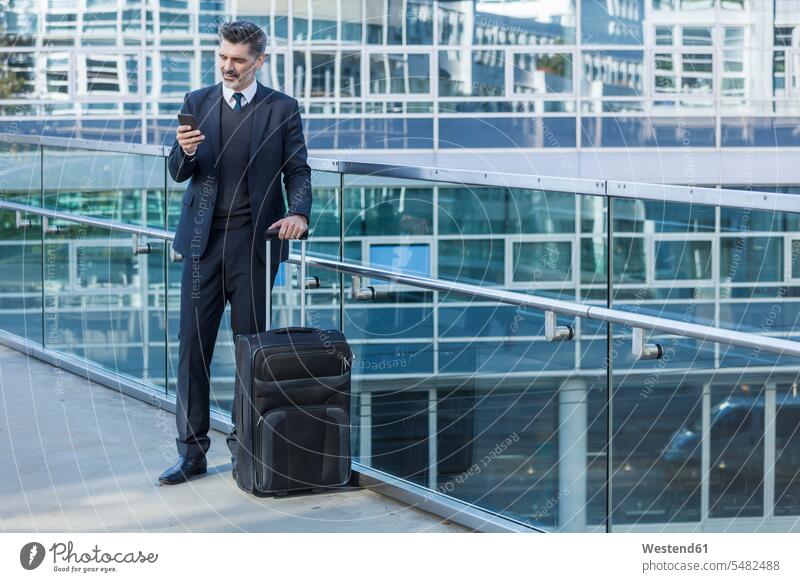 Businessman with cell phone standing with suitcase on bridge Business man Businessmen Business men suitcases Business Trip executive travel Business Trips