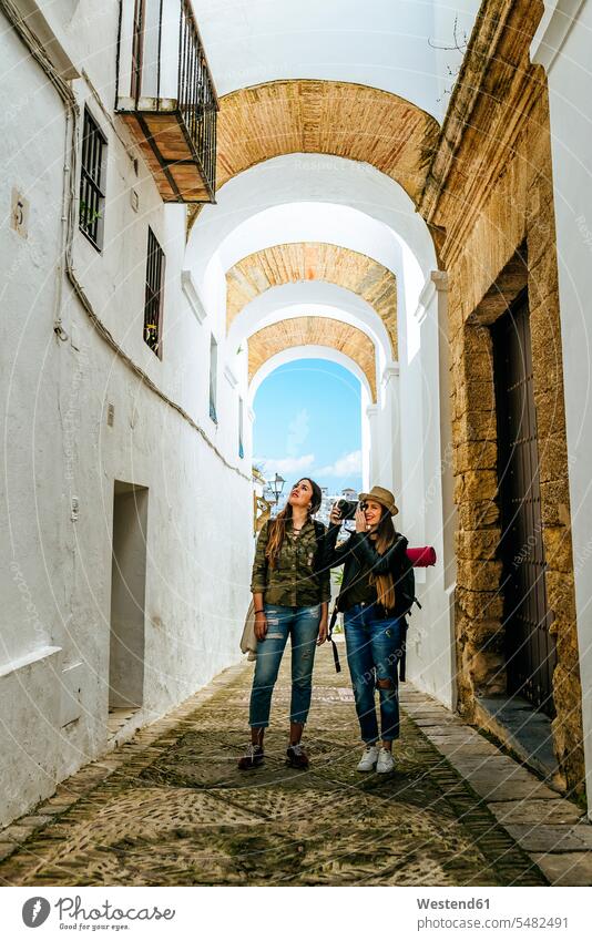 Spain, Andalusia, Vejer de la Frontera, two young women taking a photo in the alley El Callejon de las Monjas female friends lane Laneway photographing mate