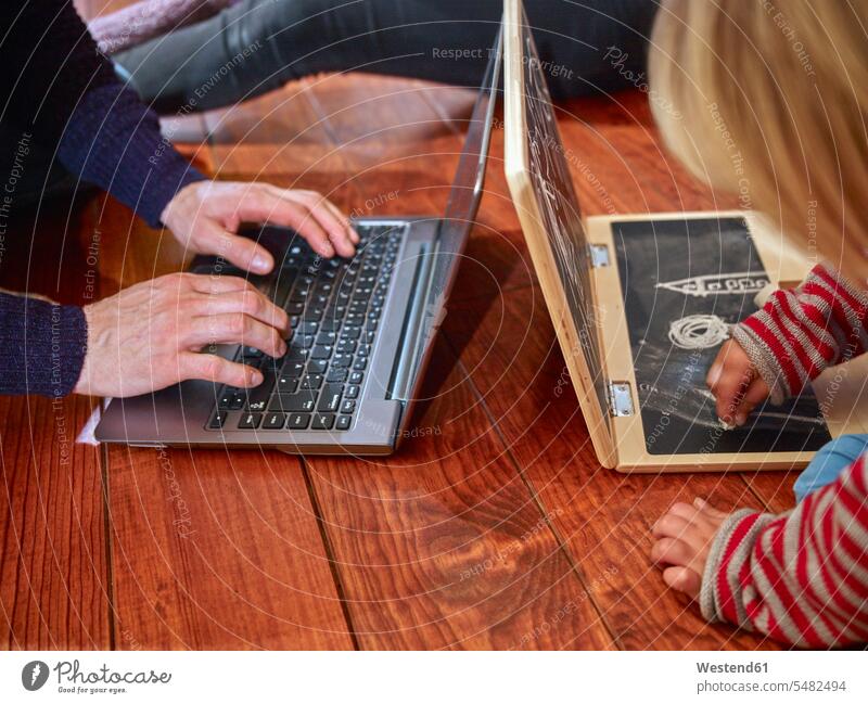 Father using laptop sitting on floor with daughter drawing on toy laptop caucasian caucasian ethnicity caucasian appearance european imitation imitate imitating