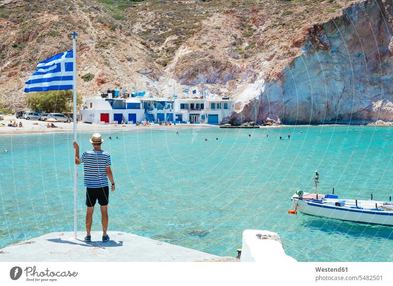 Greece, Milos, Firopotamos Beach, man looking at sea, holding onto Greek flag tourist tourists men males beach beaches vacation Holidays standing flags tourism