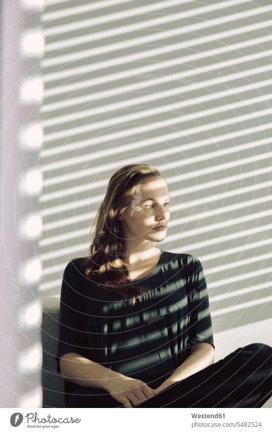 Portrait of serious young woman sitting in a shadowed room portrait portraits sunblind sun-blind jalousie venetian blind venetian blinds females women Adults