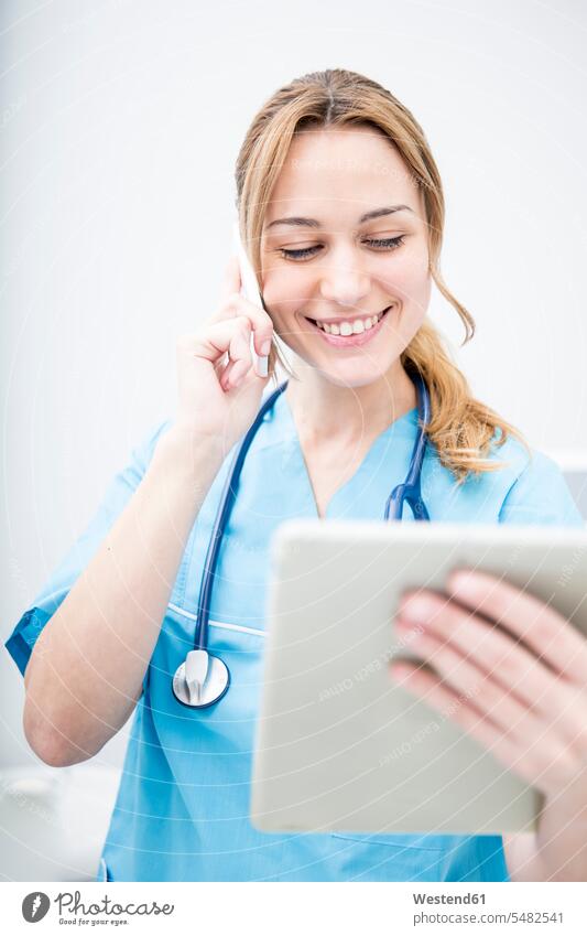 Smiling doctor on the phone looking at tablet mobile phone mobiles mobile phones Cellphone cell phone cell phones woman females women smiling smile