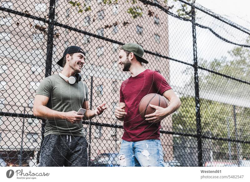 Two smiling friends with basketball outdoors man men males basketballs Fun having fun funny Adults grown-ups grownups adult people persons human being humans