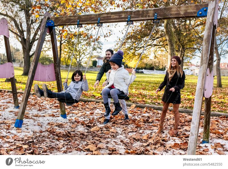 Happy family having fun with swings in autumn fall families swing set playground swing swingset people persons human being humans human beings park parks