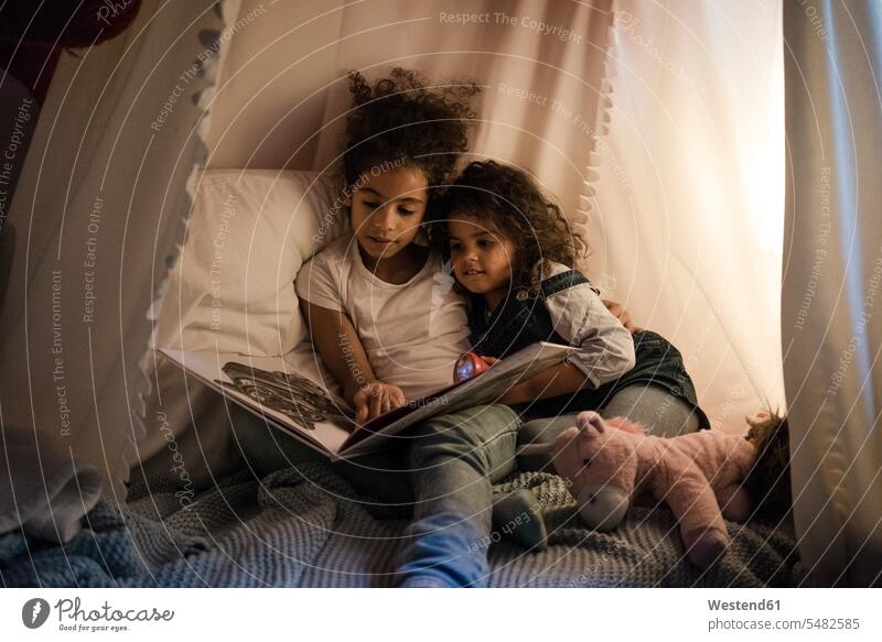 Two sisters sitting in dark children's room, reading a book books reading out read out playing Kids Room nursery child's room Seated siblings brother and sister