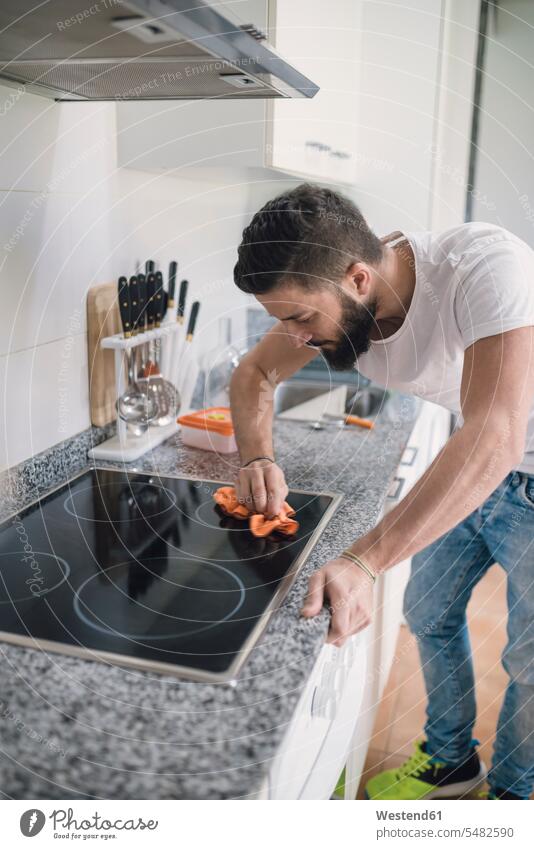 Young man cleaning ceramic hob men males kitchen Adults grown-ups grownups adult people persons human being humans human beings Household single singles