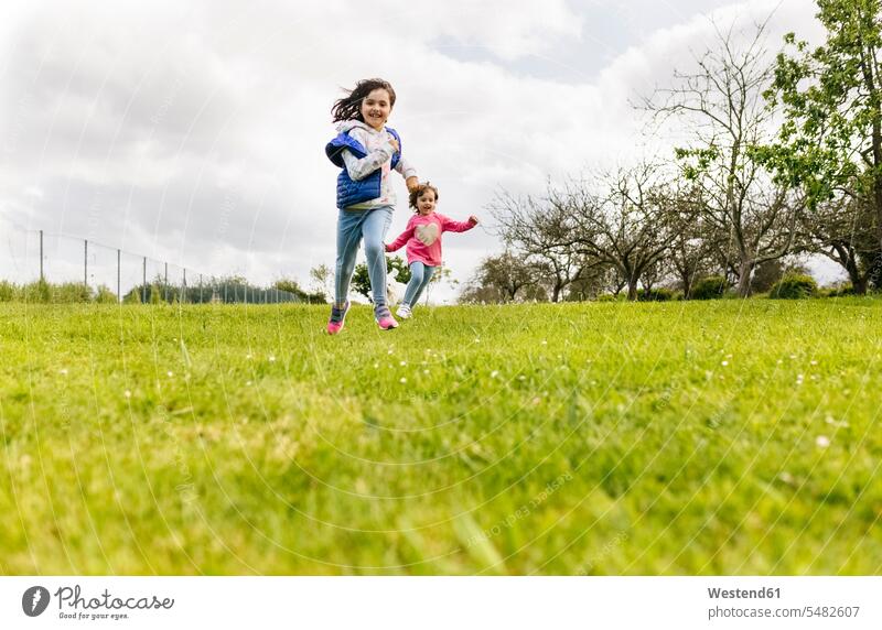 Two girls running on a meadow females sister sisters child children kid kids people persons human being humans human beings siblings brother and sister