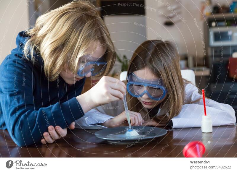 Two children wearing safety glasses using chemistry set at home experiment experimenting attempt pipette dropper pipets pipettes watching looking looking at