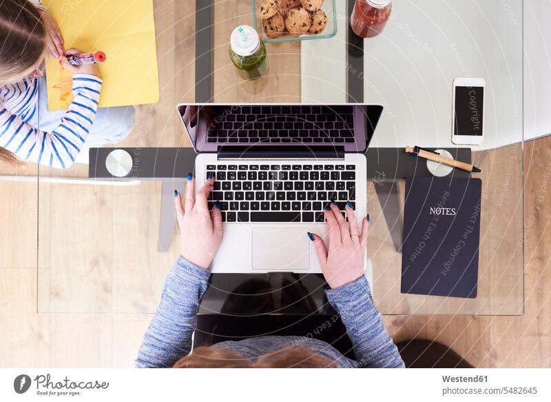 Woman typing on laptop at glass table while little girl drawing picture beside, top view mother mommy mothers mummy mama parents family families people persons