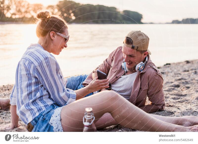 Young couple relaxing at the riverbank relaxed relaxation mobile phone mobiles mobile phones Cellphone cell phone cell phones smiling smile twosomes partnership